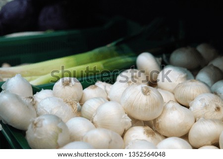 White fresh onions lying on the shelf next to the leek in the vegetable shop.