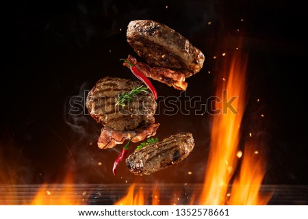 Flying beef hamburgers pieces above burning grill grid, isolated on black backround. Barbecue and grill concept