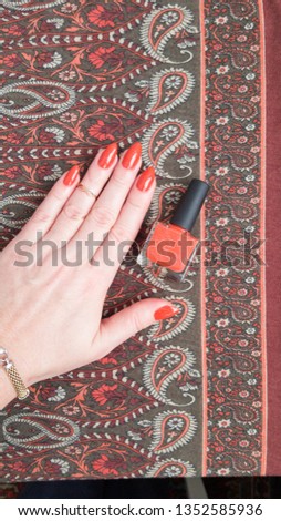 Female hand with long nails and a bottle with orange red nail polish