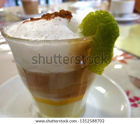 a typical spanish cafe called Zaperoco, in a glass with milk foam, cinnamon, lemon peel.picture in close view