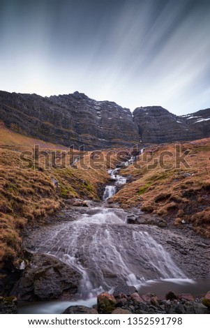 Epic vertical landscape Picture on one of thousands waterfalls and water cascadesfalling from high cliffs to moorland in the Faroe islands taken by slow shutter speed in cloudy spring and rainy day. 