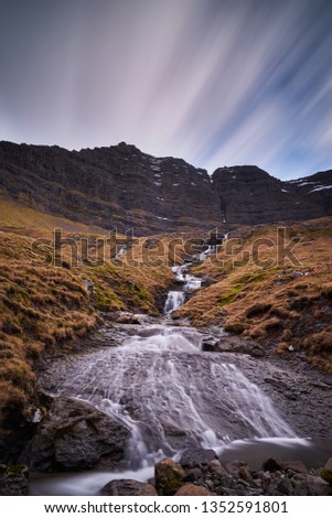 Epic vertical landscape Picture on one of thousands waterfalls and water cascadesfalling from high cliffs to moorland in the Faroe islands taken by slow shutter speed in cloudy spring and rainy day. 
