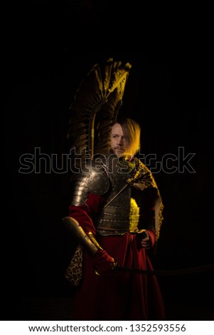 A man in vintage armor with wings of a flying legion of gussars in yellow light against a dark background.