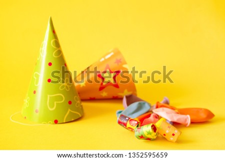Birthday paper caps, balloons, colored party whistle on yellow background