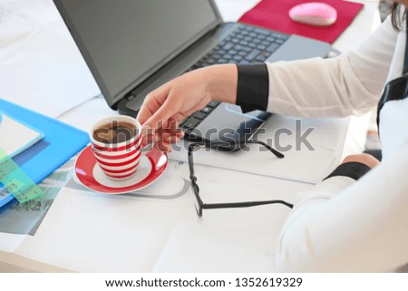 Young business woman sitting at desk with modern laptop and drinking coffee. Image