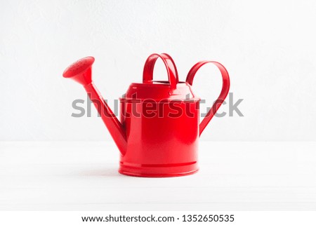 Red gardening metal watering can on white textured background with copy space