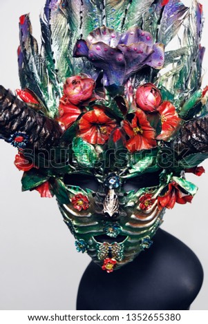 Closeup studio shot of creative facial mask with horns decorated with feathers and flowers, isolated on white background