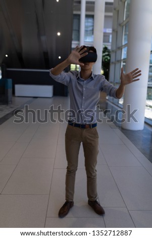 Front view of young Asian male executive using virtual reality headset standing in modern office
