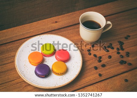Vintage photography style of colorful Macaron in white ceramic plate and a cup of coffee on wooden table top, selected focus.