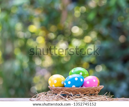 Colorful  hand  made  Easter  eggs  in  basket  on  wooden  surface  with  nature  blurry  background
