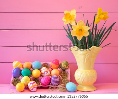 Colorful Easter Eggs in Carton with Vintage Yellow Vase filled with Spring Daffodils against Bright Pink Wood Board Background with space for copy, text or words.  Horizontal