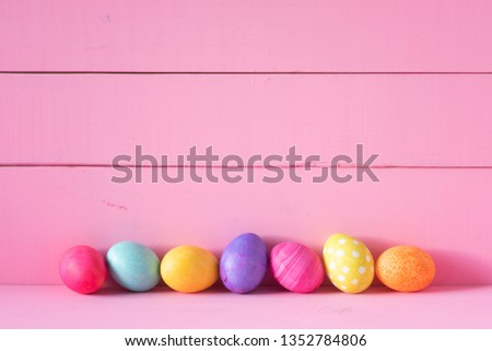 Colorful Easter Eggs in a Row on a Table and against a Bright Pink Board Wall Background with copy space. Horizontal and wide with side view