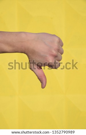 Hand of an adult male on yellow background. Gesture of the hand - finger down, not acceptance, bad, refuse.