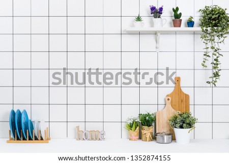 Various kinds of kitchen tools arranged on the white table. And tidy flower pots are placed neatly on the shelf.