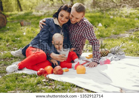 Family sitting in a park. Mother and father sitting in a summer forest with little son. Couple with child sit on a plaid. People with phone