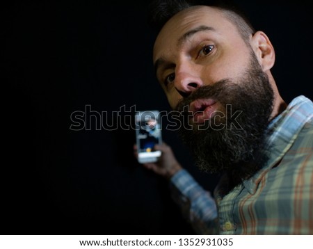 stylish man with a beard and mustache looks into the phone and makes a selfie on a black background