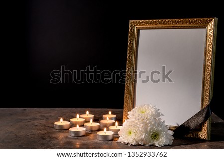 Blank funeral frame, candles and flowers on table against black background Royalty-Free Stock Photo #1352933762