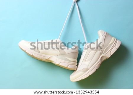 
Modern trendy sneakers hang on laces on a colored background. Casual shoes, sports shoes. Place to insert text.