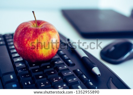 Red apple over a black keyboard in a desk as a representation of balance between healthy habits  and proffessional life.
