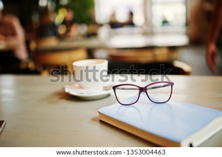 Close up photo of notebook with glasses against cup of coffe at cafe table. Eyewear concept.