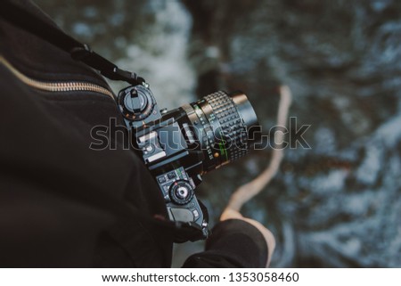 Vintage film camera around woman neck while she holds a stick into a river.