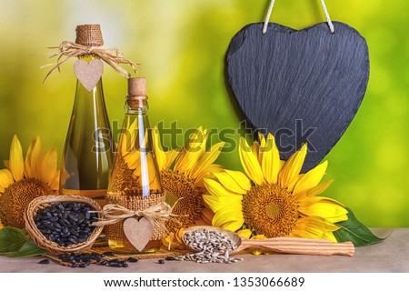 Rural still-life - sunflower oil in bottles with flowers of sunflower (Helianthus annuus) and schist black heart, closeup