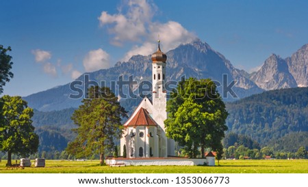 Bavarian landscape - view of the church of St. Coloman on the background of the Alpine mountains in summer day, Germany