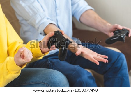 Cropped photo of two unrecognizable people in stylish and trendy casual wear playing in games using joystick and sitting on comfort sofa