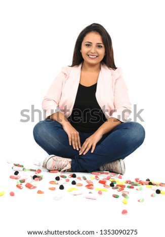 Happy young arab woman sitting on the floor while playing with different kinds of candy against a white background