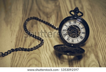 Antique pocket watch with a noticeable mechanism and Latin numerals on a wooden desk