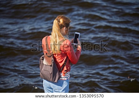 The girl in the red jacket photographs the water in the river on the phone