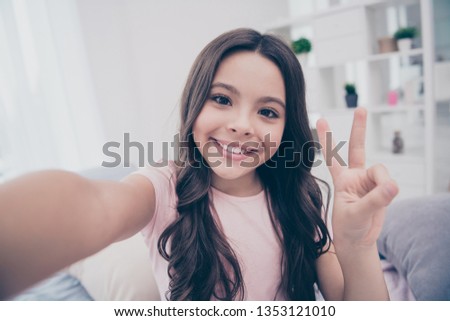 Close up photo cute beautiful  little girl smart phone hands take selfies show v-sign say hi curly wavy wear home t-shirt pants comfortable apartments flat bright light colored room