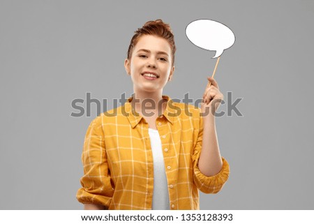 photo booth, party props and people concept - smiling red haired teenage girl in checkered shirt holding blank speech bubble over grey background Royalty-Free Stock Photo #1353128393