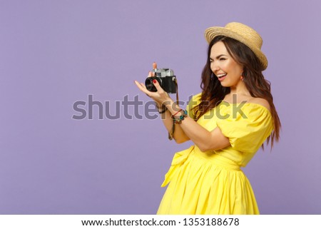 Cheerful young woman in yellow dress hat taking picture on retro vintage photo camera looking aside isolated on pastel violet background. People sincere emotions lifestyle concept. Mock up copy space