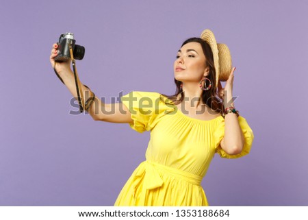 Stunning young woman in yellow dress, summer hat doing selfie on retro vintage photo camera isolated on pastel violet wall background. People sincere emotions, lifestyle concept. Mock up copy space