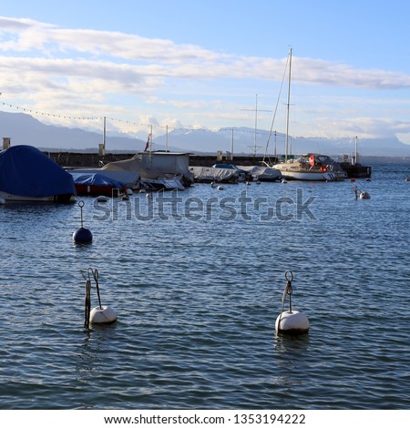Beautiful landscape photographed in picturesque town of Nyon, Switzerland. In this photo you can see relatively calm lake, blue sky with some clouds, different kinds of boats and buoys. Relaxing view!