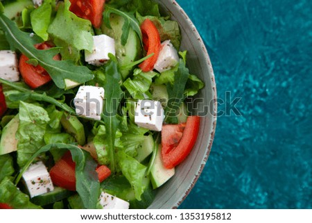 fresh vegetarian salad in a plate: lettuce, cucumber, avocado, tomato, feta cheese, arugula, spices and herbs. Healthy food