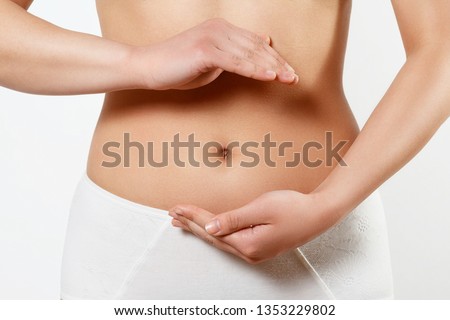 Close up cropped photo of beautiful woman's slim stomach, using hands she is showing a balance. The concept of healthy eating, diet. Early pregnancy. on white background Royalty-Free Stock Photo #1353229802