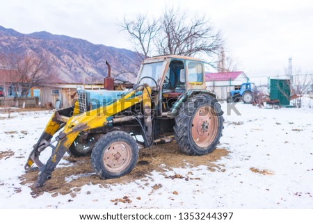 Tractor in the backyard of a rural home. Old tractor in the village in winter. Agriculture household in the mountain region. Agricultural transport in the country.