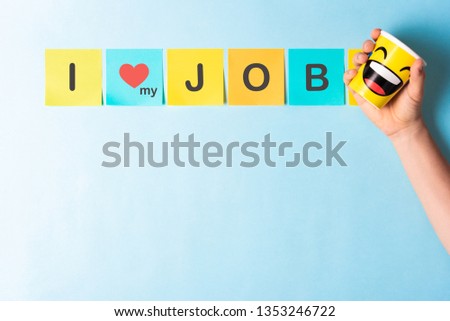 Concept of "I love my job" with multicolored sticky notes and hand holding a paper cup with happy smile cartoon on blue background and blank space for text