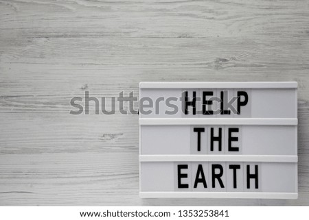 'Help the Earth' words on modern board over white wooden surface, top view. Flat lay, overhead, from above. Copy space.
