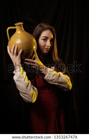 Girl in medieval dress and cloak in yellow light against a dark background