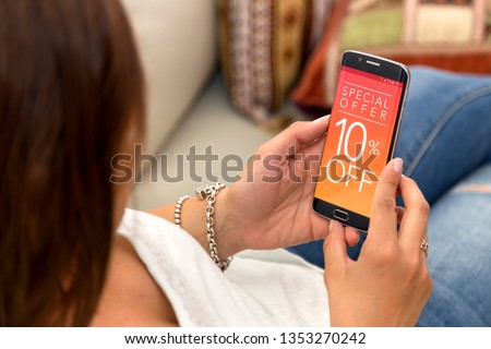 10 off Promotion, special offer in a cell phone. One young woman in her home resting in sofa holding a smartphone with a advertising 10% off  in the screen.