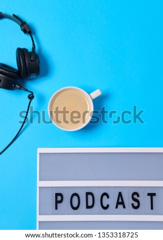 Music  background with Podcast word on lightbox,  headphones and cup of coffee on blue table, flat lay. Top view, flat lay, space for text