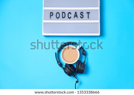 Music  background with Podcast word on lightbox,  headphones and cup of coffee on blue table, flat lay. Top view, flat lay, space for text