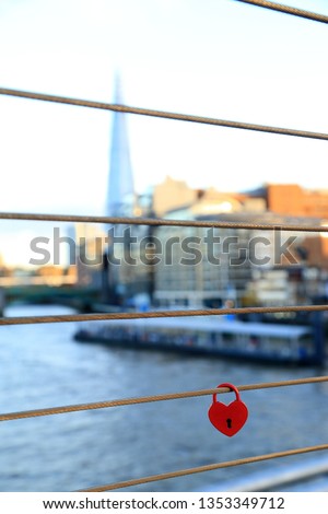 Red heart padlock on a fence bridge as love symbol with blurred scene of the river.