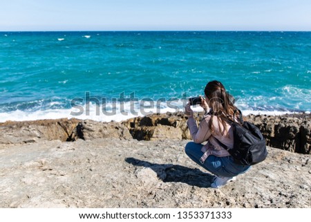 Woman crouching taking pictures of shore with smart phone