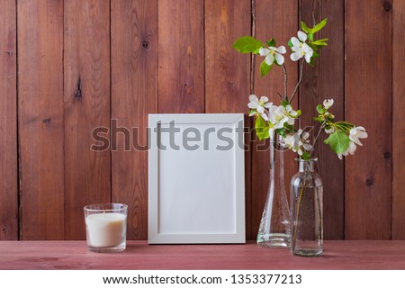 Mockup with a white frame and white spring flowers in a vase on a wooden table
