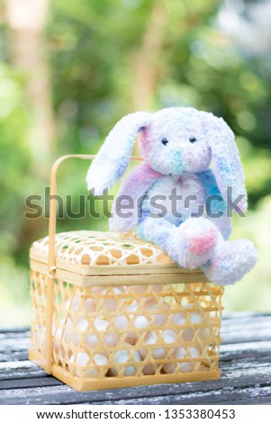 a colorful easter bunny rabbit and white eggs in a wooden basket with green nature background