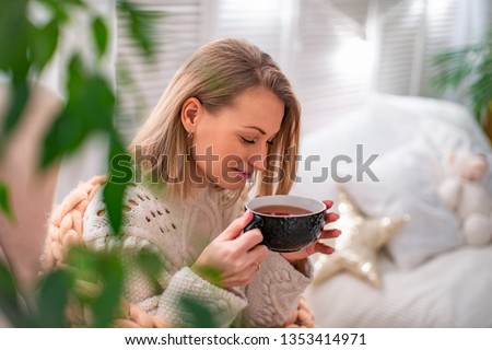 blonde girl in a sweater with a Cup of tea sitting on the bed